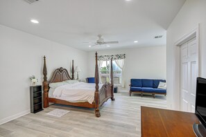 A bedroom with a four-poster bed, a blue sofa, and a television. - Waveland Vacation Rental - Walk to the Beach! (Waveland)