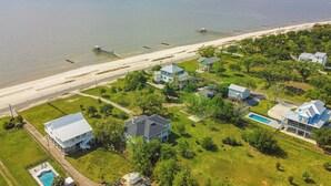 Vue aérienne d’une zone résidentielle côtière, avec des maisons, une plage et une jetée.