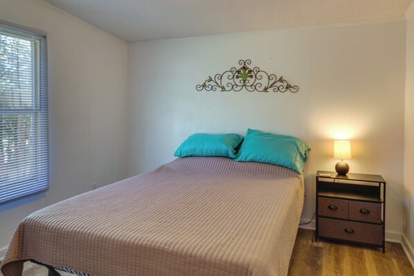 A bedroom with a bed, two pillows, a nightstand with a lamp, and a decorative wall piece. - Prosperity Vacation Rental ~ 1 Mi to Lake Murray! (Prosperity)
