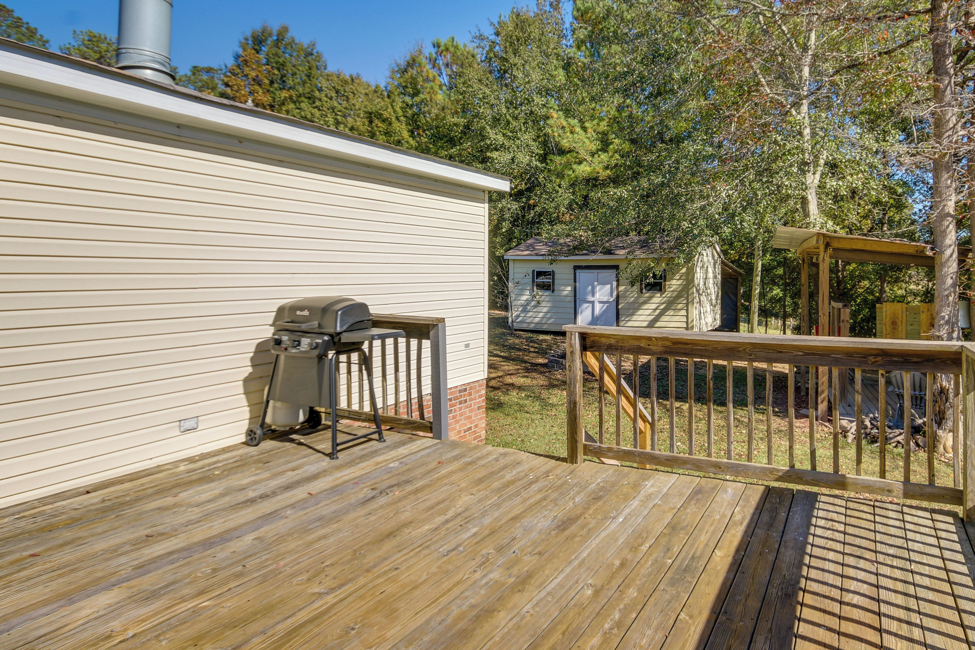 Une terrasse en bois avec un barbecue et un petit abri de jardin en arrière-plan.