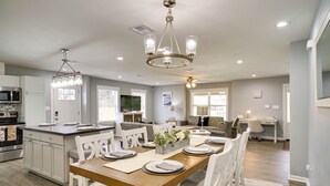 A spacious kitchen with a central island, white cabinetry, and a dining area with a wooden table set for four. - Lake Charles Home w/ Gas Grill & Fenced-in Yard! (Lake Charles)