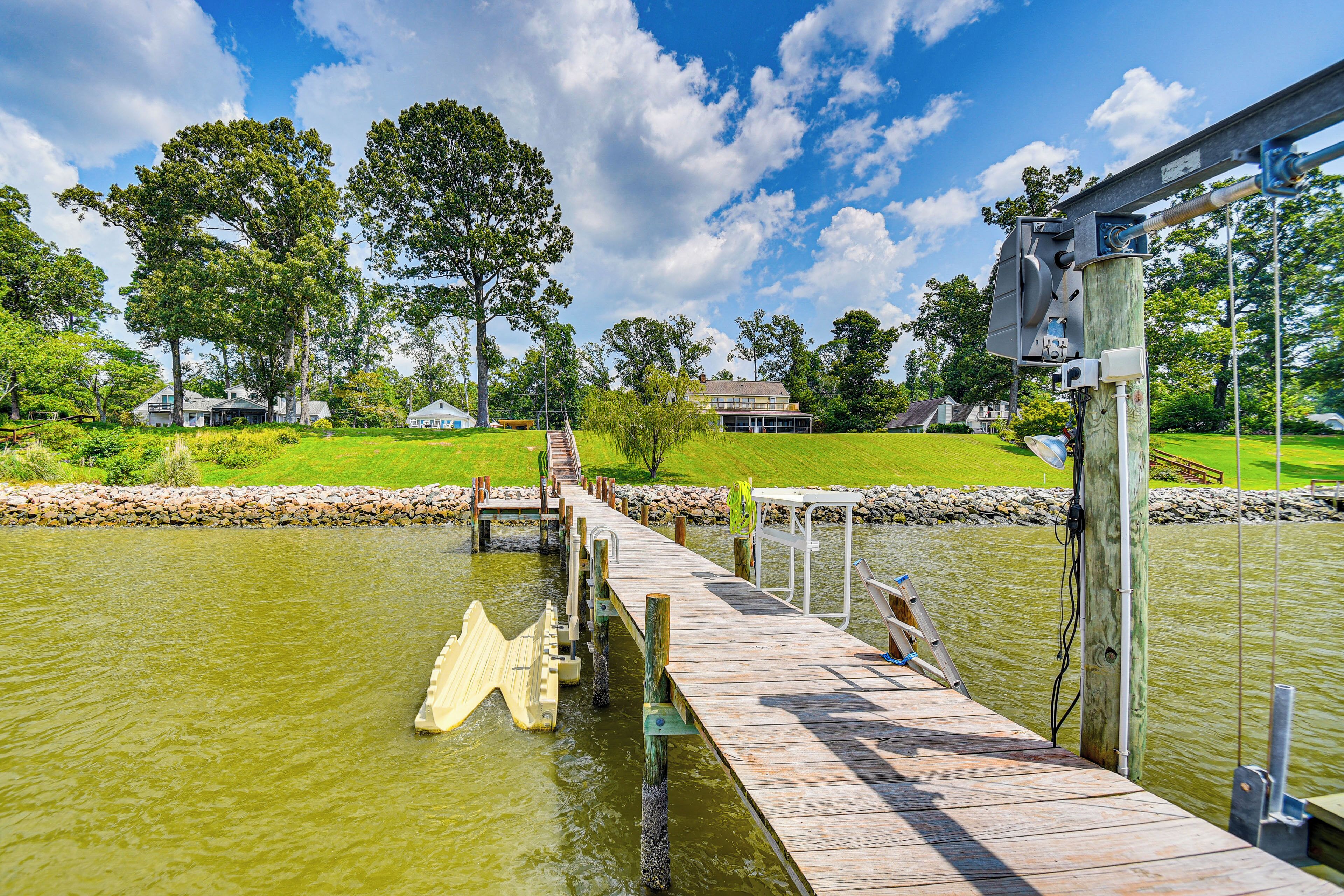 Eine Holzstege führt ins Wasser, mit blauem Himmel und Bäumen im Hintergrund.