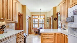 A kitchen with wooden cabinets, a dishwasher, and a refrigerator. There is a window with a view of trees and a chandelier hanging from the ceiling. - Eau Claire Retreat: Close to Campus & Dtwn! (Eau Claire)