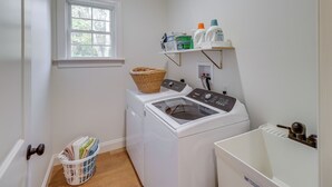 A laundry room with a front-loading washer and dryer, a basket, shelves with laundry supplies, and a window.