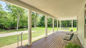 A covered porch with a wooden deck, white columns, and a view of a grassy yard and trees.