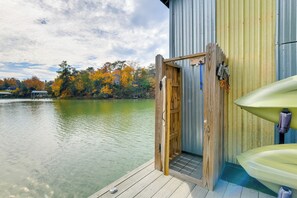 A wooden deck with a kayak and a covered area, overlooking a calm lake with autumn trees in the background.