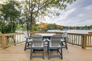Eine Terrasse mit Tisch und Stühlen mit Blick auf einen See, umgeben von Bäumen und einem Holgitter.