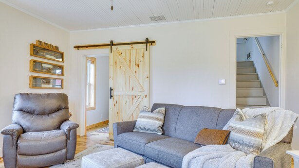 A living room with a grey sofa, a leather armchair, and a wooden barn door. - Lovely Rural Hixton Farmhouse w/ Porch & Fire Pit! (Hixton)