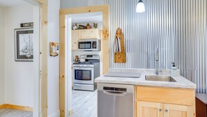 A modern kitchen with wooden cabinets, a built-in microwave, a dishwasher, and a wooden hanging rack. - Lovely Rural Hixton Farmhouse w/ Porch & Fire Pit! (Hixton)