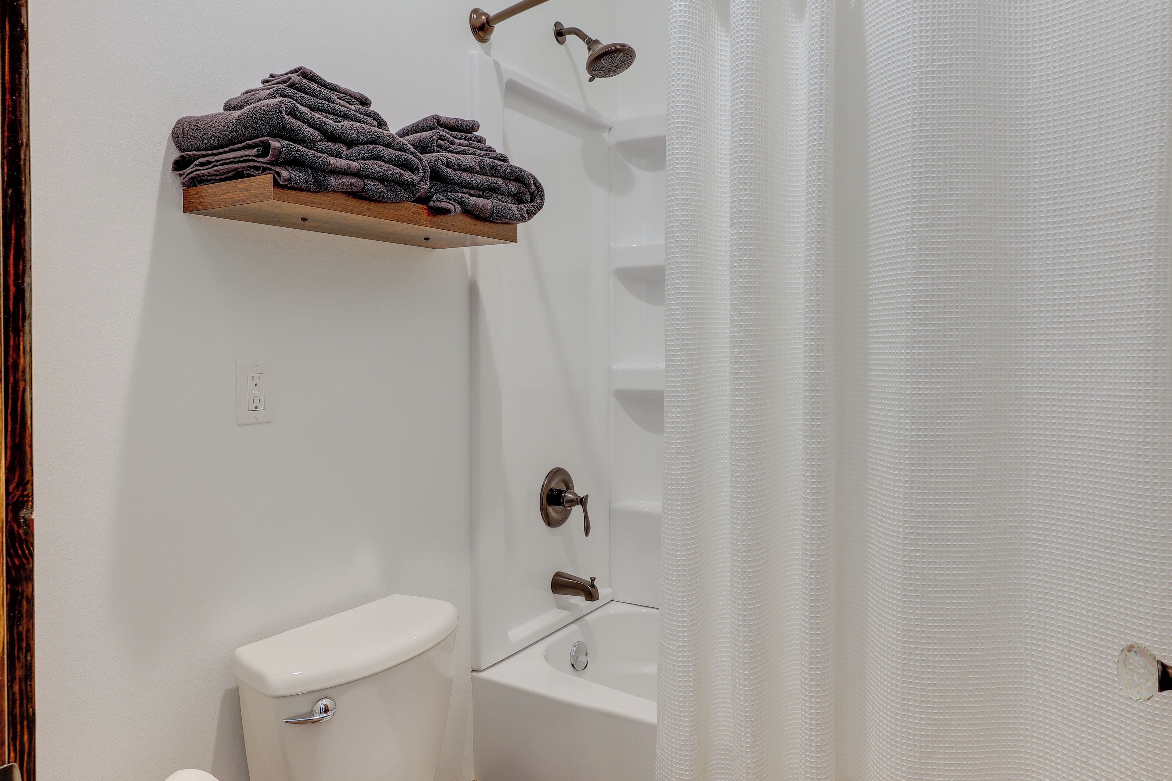 A bathroom with a toilet, a sink, a shower, and a shelf with folded towels.