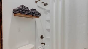 A bathroom with a toilet, a sink, a shower, and a shelf with folded towels.