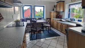 A kitchen with a dining area, featuring a tiled floor, wooden cabinets, a microwave, and a clock on the wall.