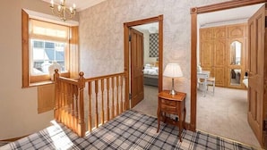 A room with a wooden staircase, a plaid carpet, a chandelier, and a view of a bedroom with a bed and a dresser. - Maxwelston Farmhouse (Girvan)