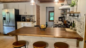 A kitchen with a wooden island, bar stools, a stainless steel refrigerator, and a stove. - Red Stone Retreat-10 Min to Asheville, Game Room, Firepit, Quiet and Secluded  (Swannanoa)