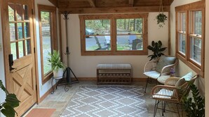 A cozy room with wooden beams, a bench, wicker chairs, and large windows. - Red Stone Retreat-10 Min to Asheville, Game Room, Firepit, Quiet and Secluded  (Swannanoa)