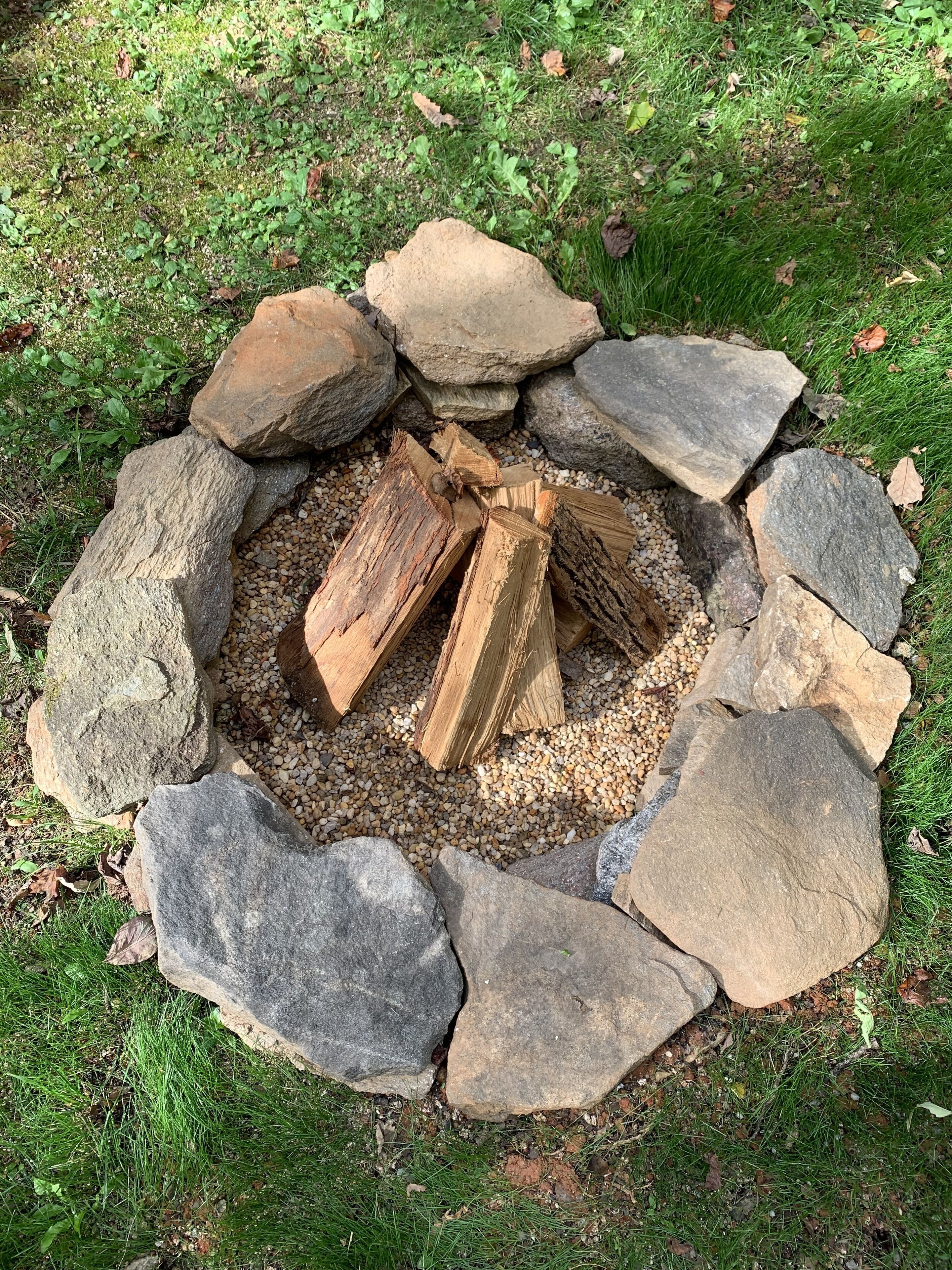A stone fire pit surrounded by logs and gravel.