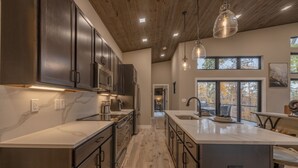 Una cocina moderna con armarios oscuros, encimera de mármol e iluminación colgante.