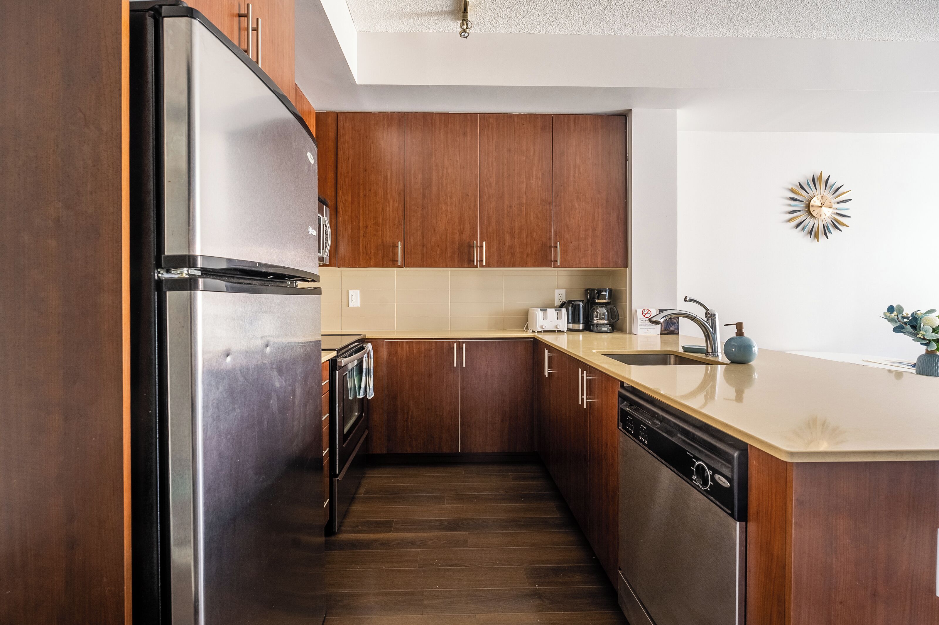 Une cuisine moderne avec des meubles en bois, des appareils en acier inoxydable et un plan de travail de couleur beige.