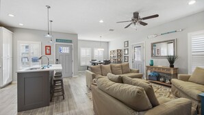 A spacious living area with a beige sofa set, a kitchen island with a sink, and a ceiling fan. - 3 Bed 2 Bath house Chasing Sunsets Sleeps 7 (panama city beach)