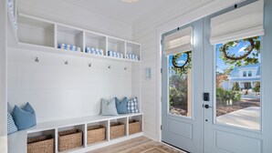Interior limpo e claro, com piso de madeira, um banco com cestos de armazenamento e uma porta com vista para o exterior.