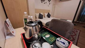 Een hotelkamer met een bed, een bureau met een dienblad waarop een waterkoker, bekers en een pak thee staan.