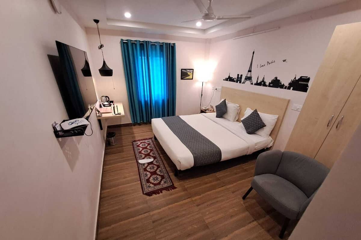 Habitación de hotel con cama, escritorio, silla, armario, espejo y un mural urbano en la pared.