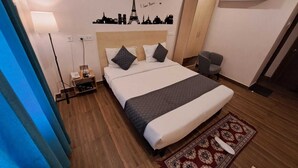 Habitació d'hotel amb un llit, una tauleta de nit, una cadira, una decoració mural de monuments de París i un aparell d'aire condicionat.