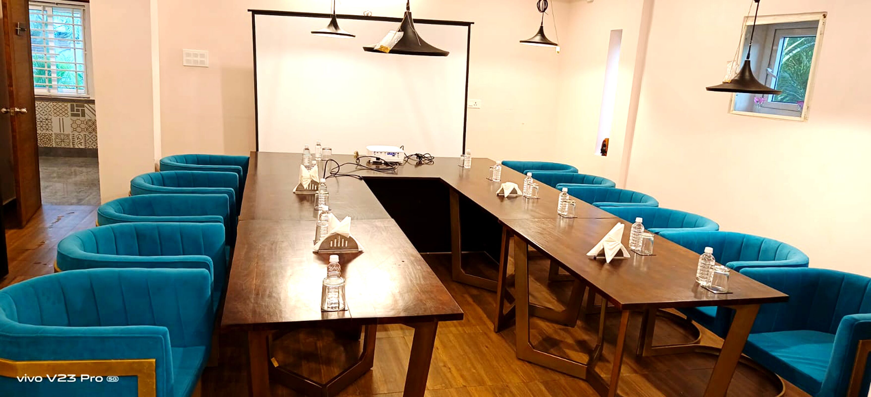 Un salón de conferencias con una larga mesa, sillas tapizadas en azul y un proyector.