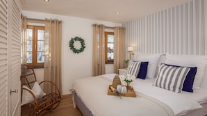 A bedroom with a large bed, a wicker chair, a bedside table with a lamp, and a window with curtains. - MY STAY: Relaxation between Chiemsee beach & Kampenwand, plenty of space with 79 sqm (Bernau am Chiemsee)
