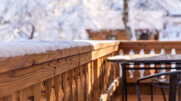 Eine Holzdielen-Terrasse mit einem mit Schnee bedeckten Geländer und einem Tisch mit Stühlen.
