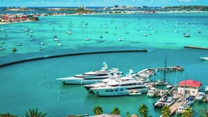 Een jachthaven met diverse jachten afgemeerd, omgeven door helder turquoise water en een kustplaats in de verte.