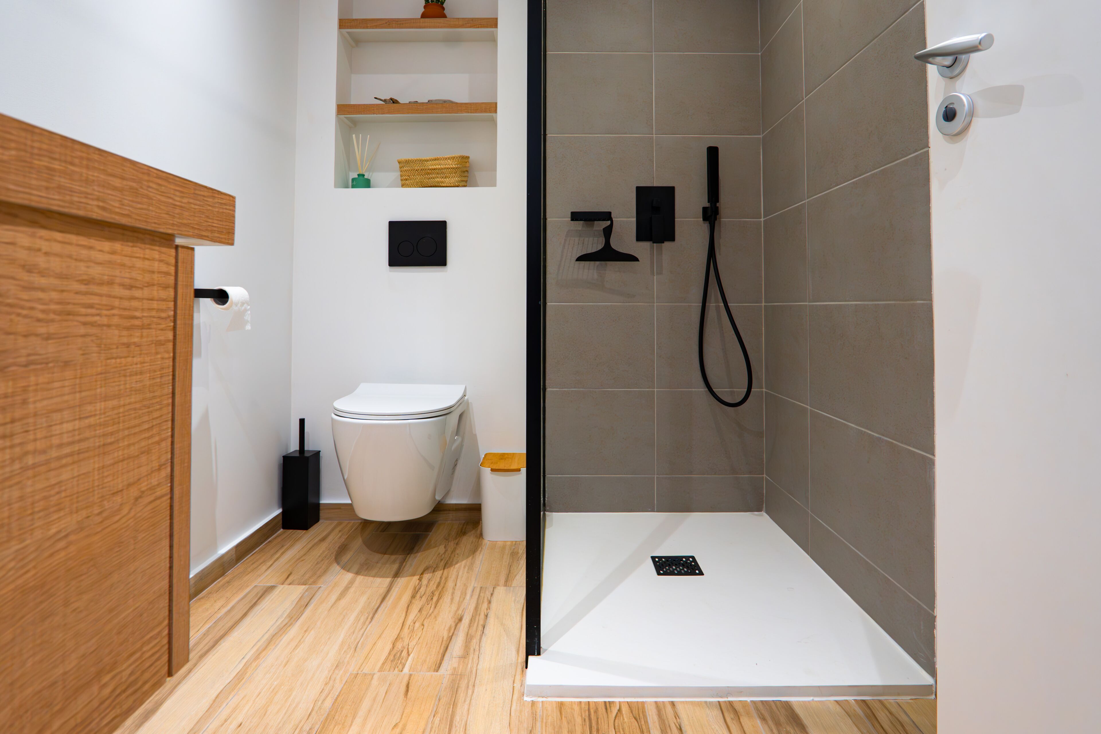 A modern bathroom with a toilet, a shower with a glass door, and a wooden vanity.