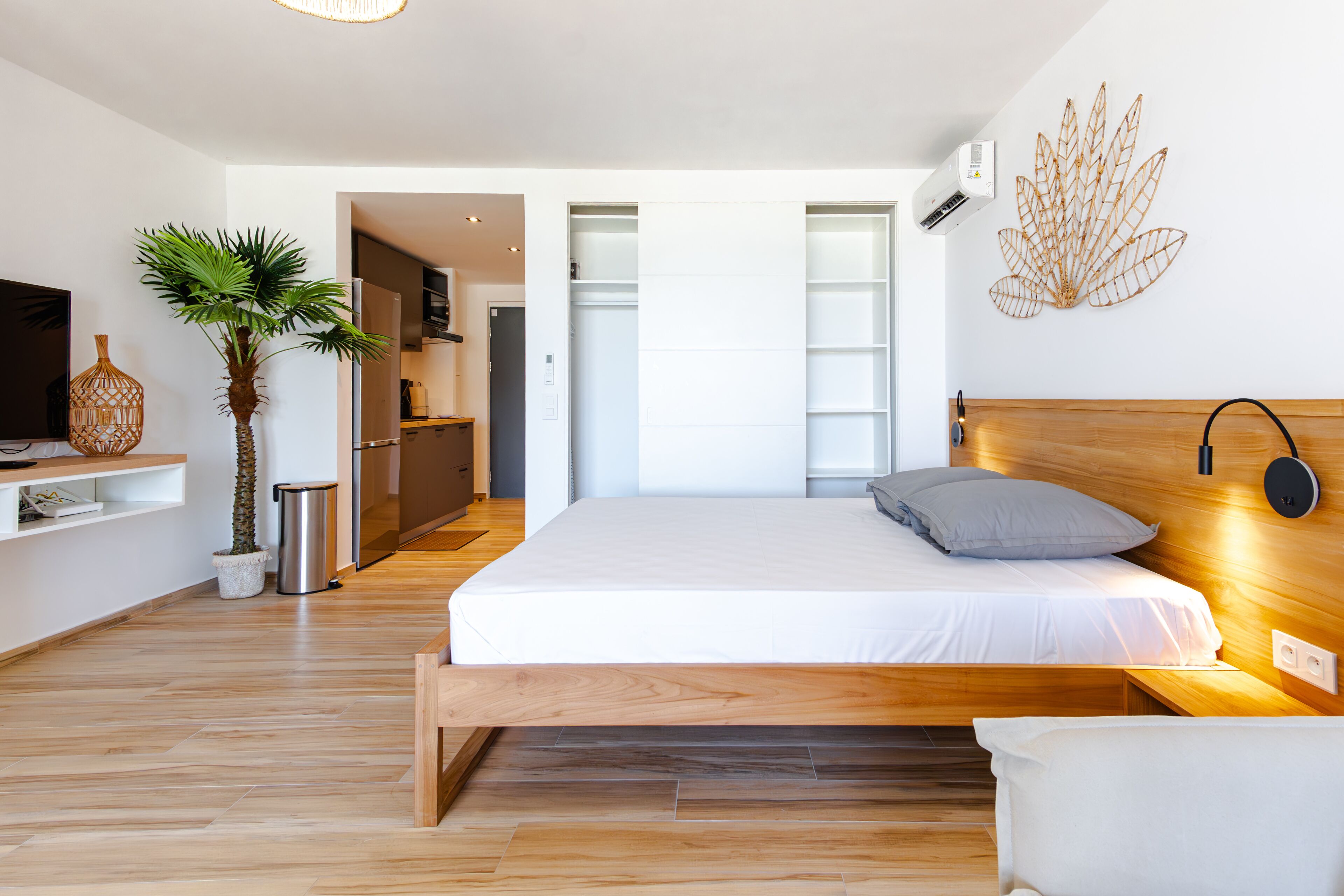 A modern bedroom with a wooden bed, a small bedside table, a potted plant, and a wall-mounted light fixture.
