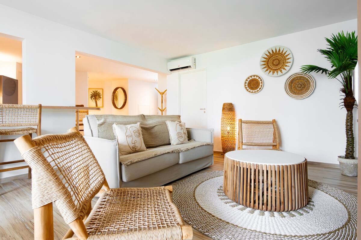 A modern living room with a sofa, wicker chairs, a round coffee table, and decorative wall art.