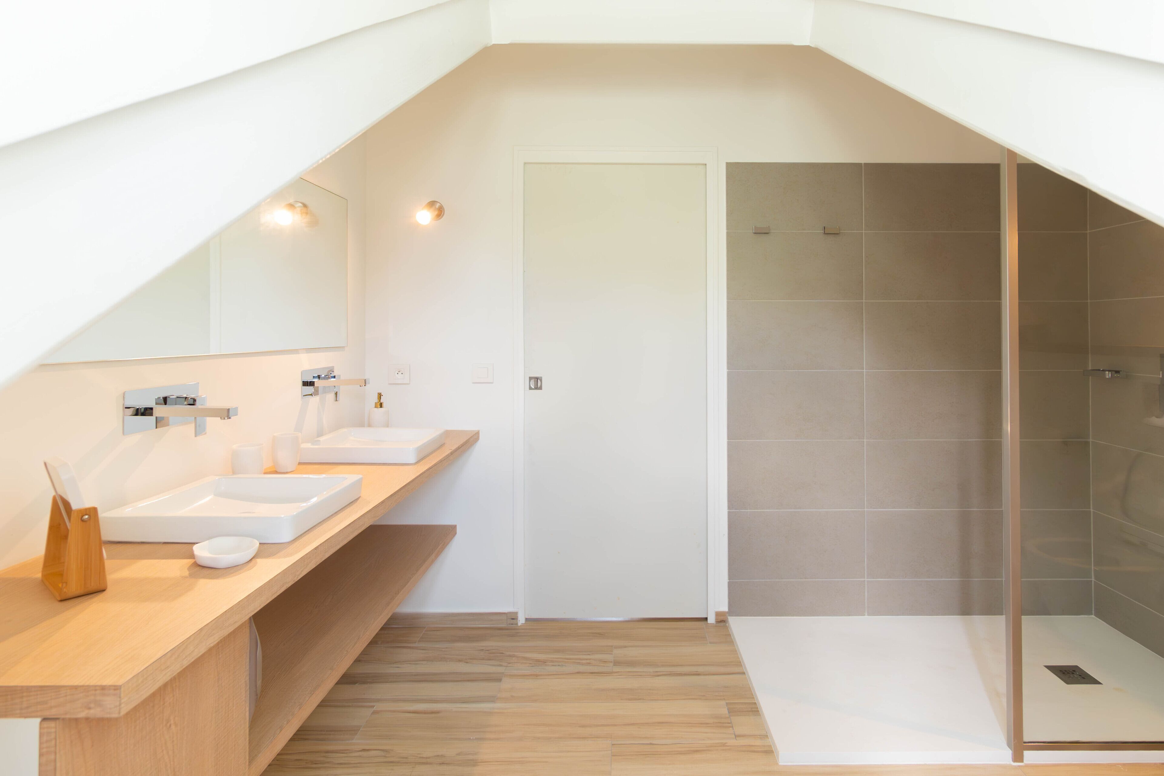 Un baño moderno con tocador de madera, dos lavamanos, cabina de ducha de vidrio y un espejo grande.