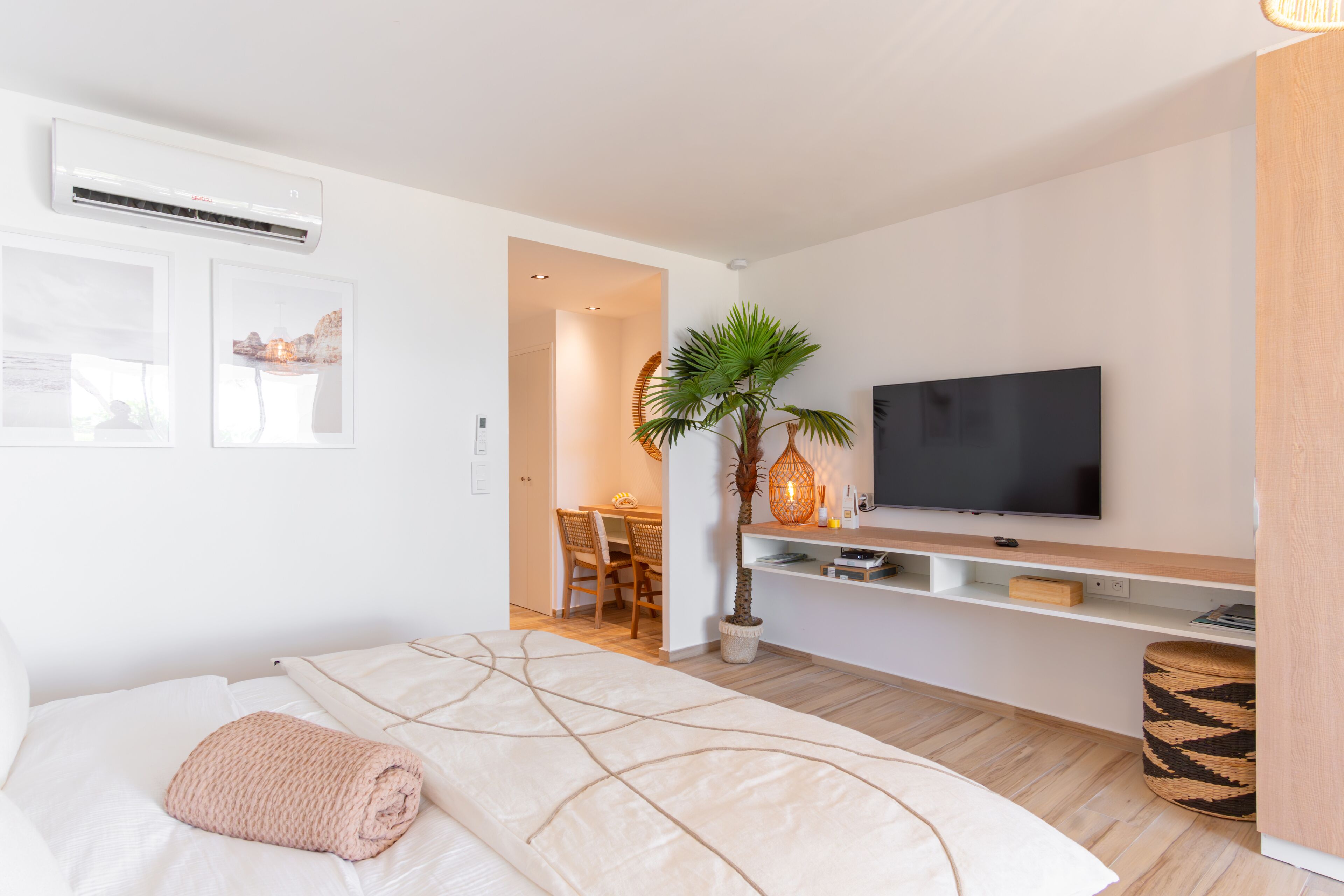 A modern hotel room with a bed, a TV, a dining area, and a potted plant.