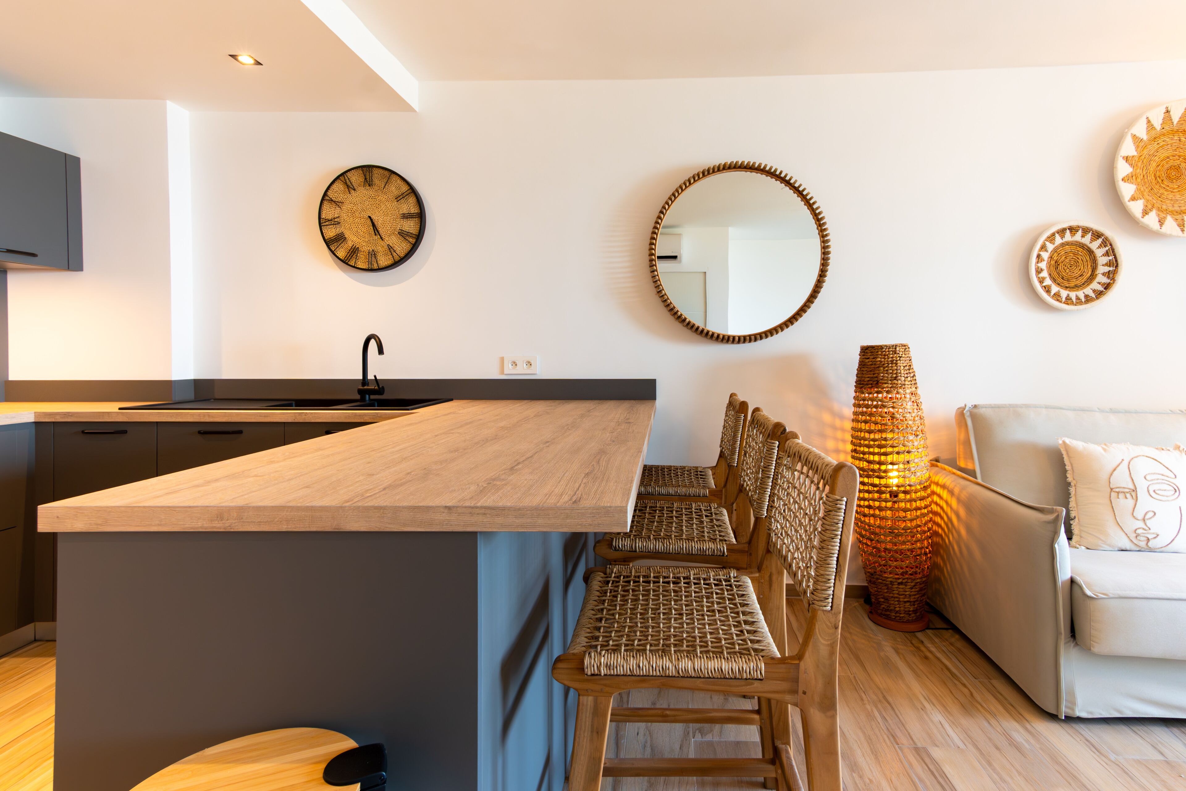 Eine moderne Küche mit einer zentralen Kochinsel, einem Essbereich mit Korbstühlen, einer Couch und dekorativen Wandbildern.