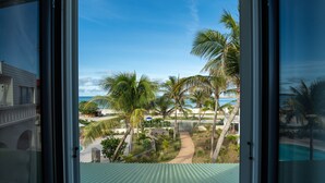 Uitzicht vanuit een raam op een tropisch resort met palmbomen, een pad en een zwembad.