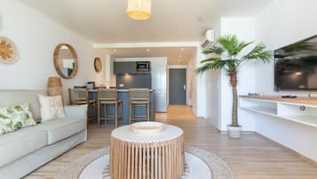 Un salon moderne avec une table basse ronde en bois, un canapé avec des coussins, un tapis tissé et un téléviseur posé sur un meuble.