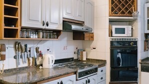 Una cocina con gabinetes blancos, estufa, microondas y pileta.