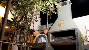 Un espacio de cocina al aire libre con un horno de piedra, rodeado de macetas con plantas y una estructura de madera rústica.