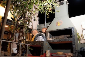 An outdoor kitchen area with a stone oven, surrounded by potted plants and a rustic wooden structure. - HOSTEL La Casa de Li  En (Chilecito)