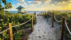 A sandy pathway leading to a beach with a wooden fence and a small structure with a green roof. - Waterfront Htd Pool, Spa, Billiards, Lanai, Canal (Delray Beach)