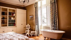 A bedroom with a large bed, a vanity with a bathtub, a small table with a chair, and a bookshelf. - Château de la Grange Moreau (Vallon-sur-Gée)