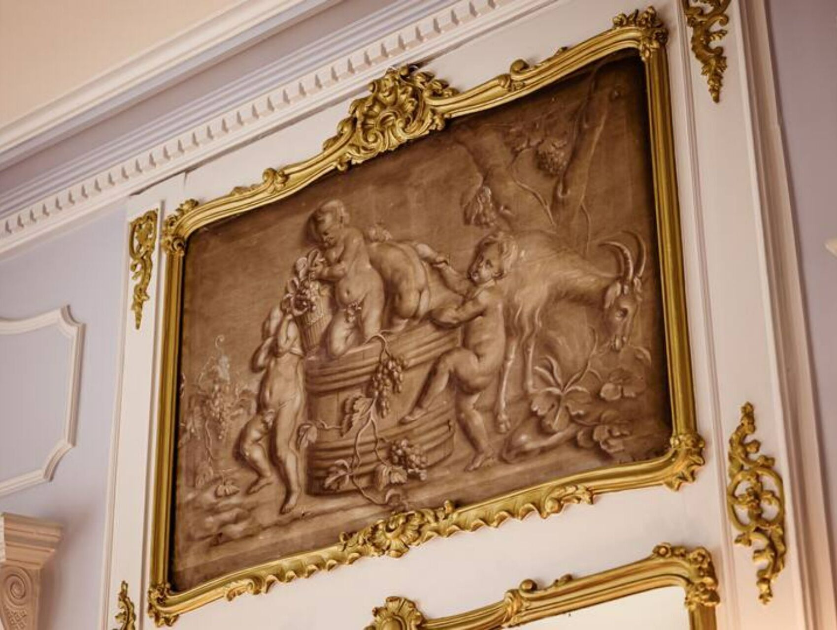 A detailed wall mural with classical figures and ornate gold framing.