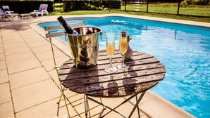 A poolside table with a bucket of champagne and two glasses, a pool, and lounge chairs in the background. - Château de la Grange Moreau (Vallon-sur-Gée)