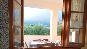 Un balcon avec une table et des chaises, une vue sur une montagne et des arbres, et un papier peint à motifs.