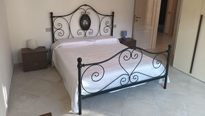 Un lit avec un cadre en métal noir, une couvre-lit blanche et une petite table de chevet avec une lampe.