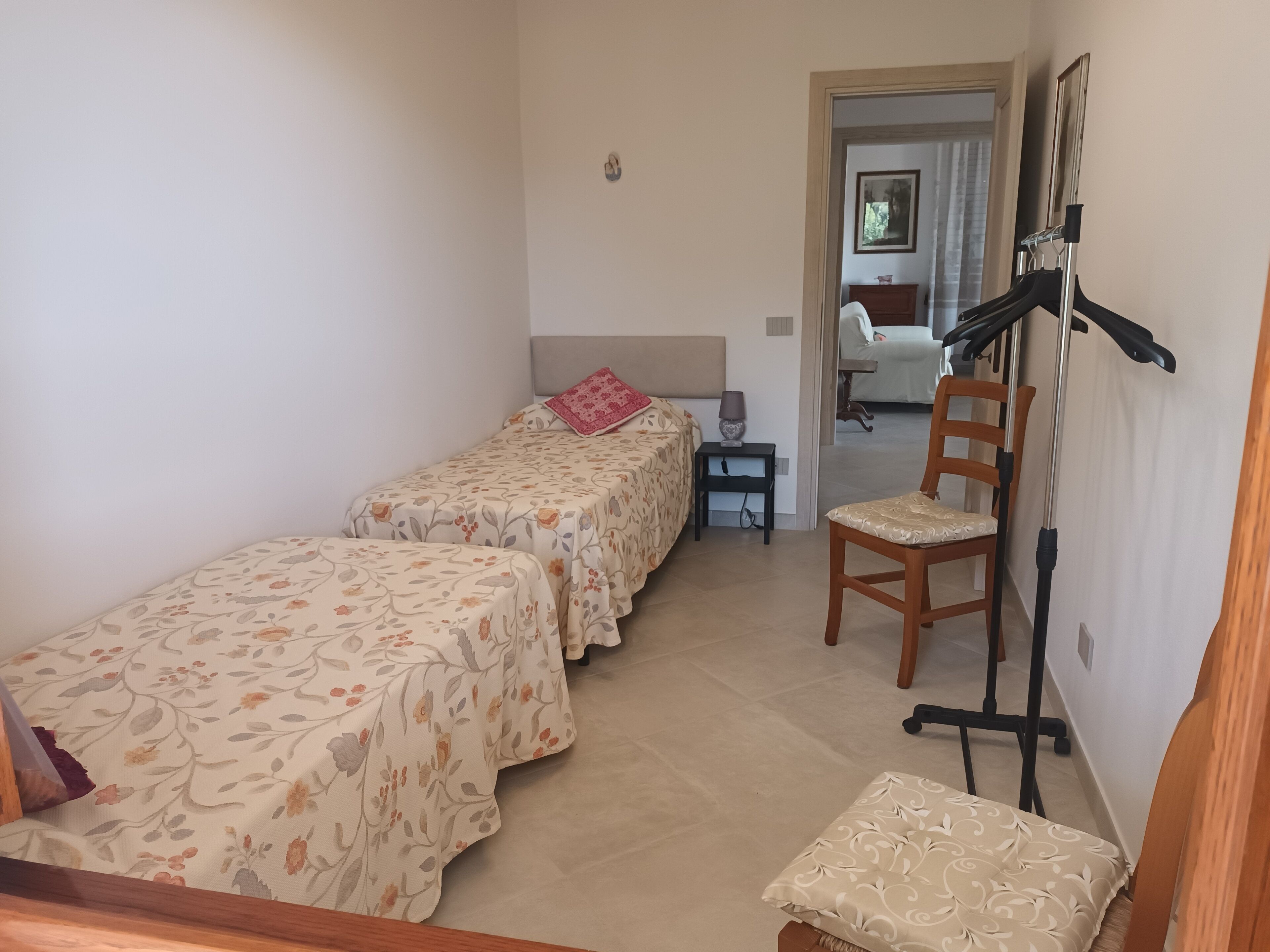 A bedroom with two single beds, a wooden chair, a small table, and a treadmill.