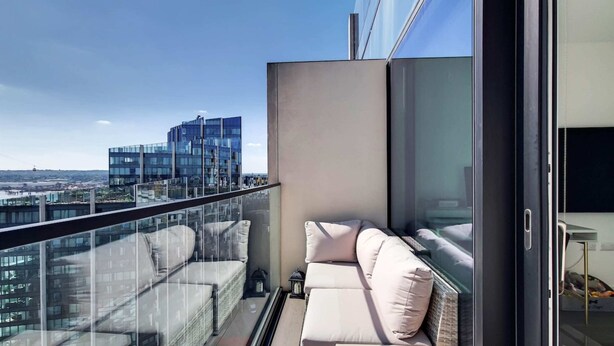 Un balcon doté d’un canapé et d’une balustrade en verre, offrant une vue sur le paysage urbain.